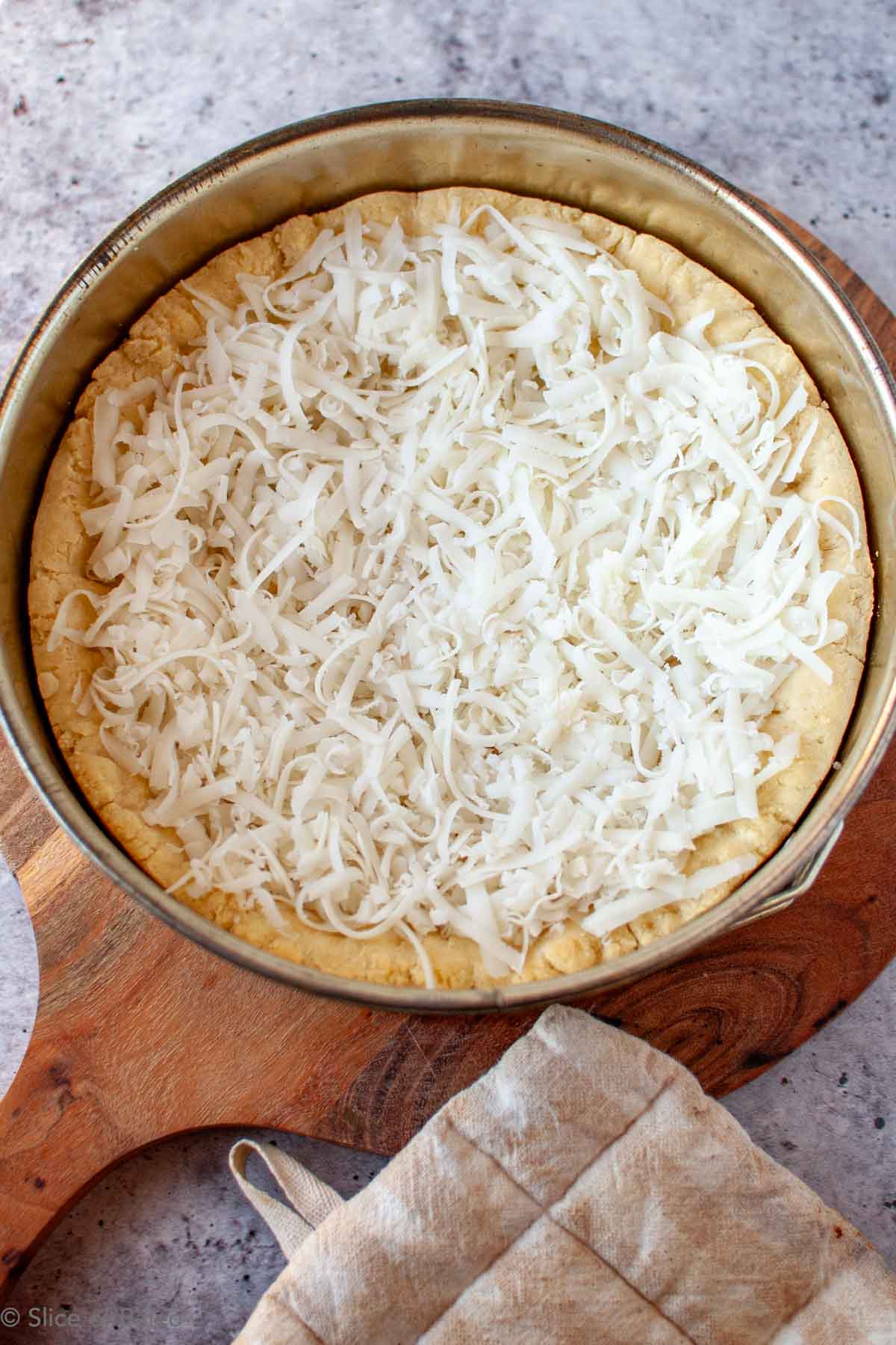 Paleo Chicago Style Deep Dish Pizza partially baked dough in a springform cake pan with shredded cheese on top.