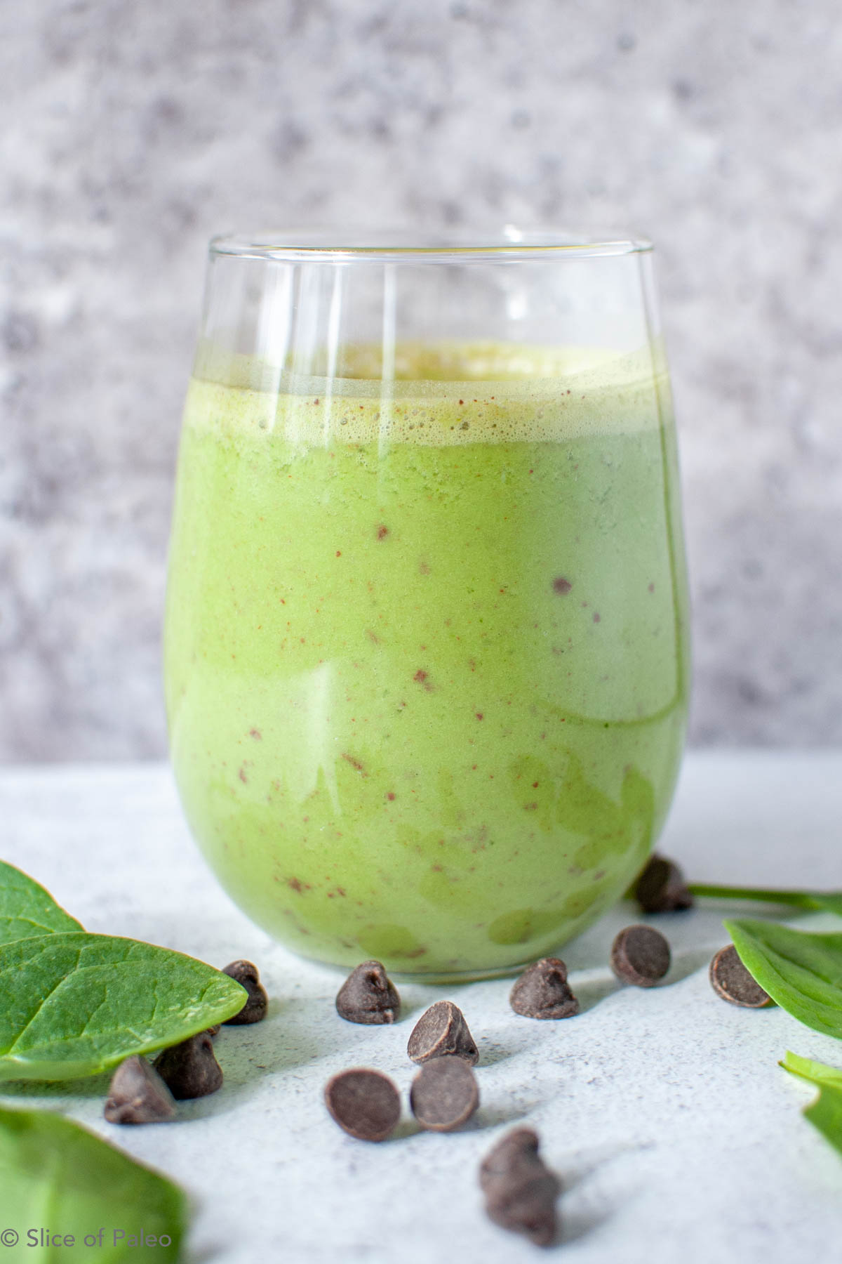 Paleo Shamrock shake in a tumbler shown with chocolate chips and spinach